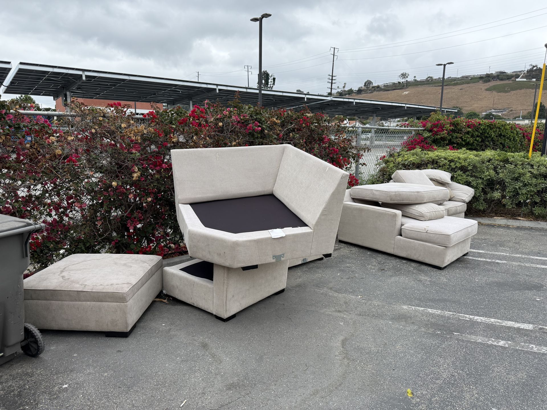 Outdoor patio seating with beige modular chairs and cushions on pavement beside flowering bushes