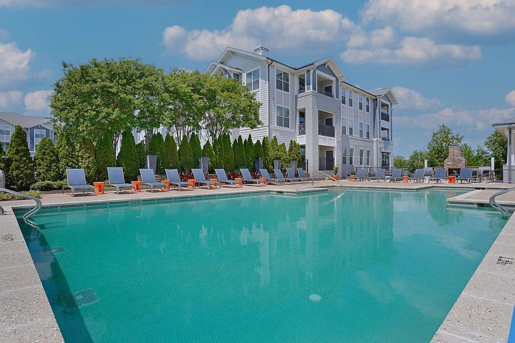Outdoor apartment pool with lounge chairs and a multi-story building in the background.