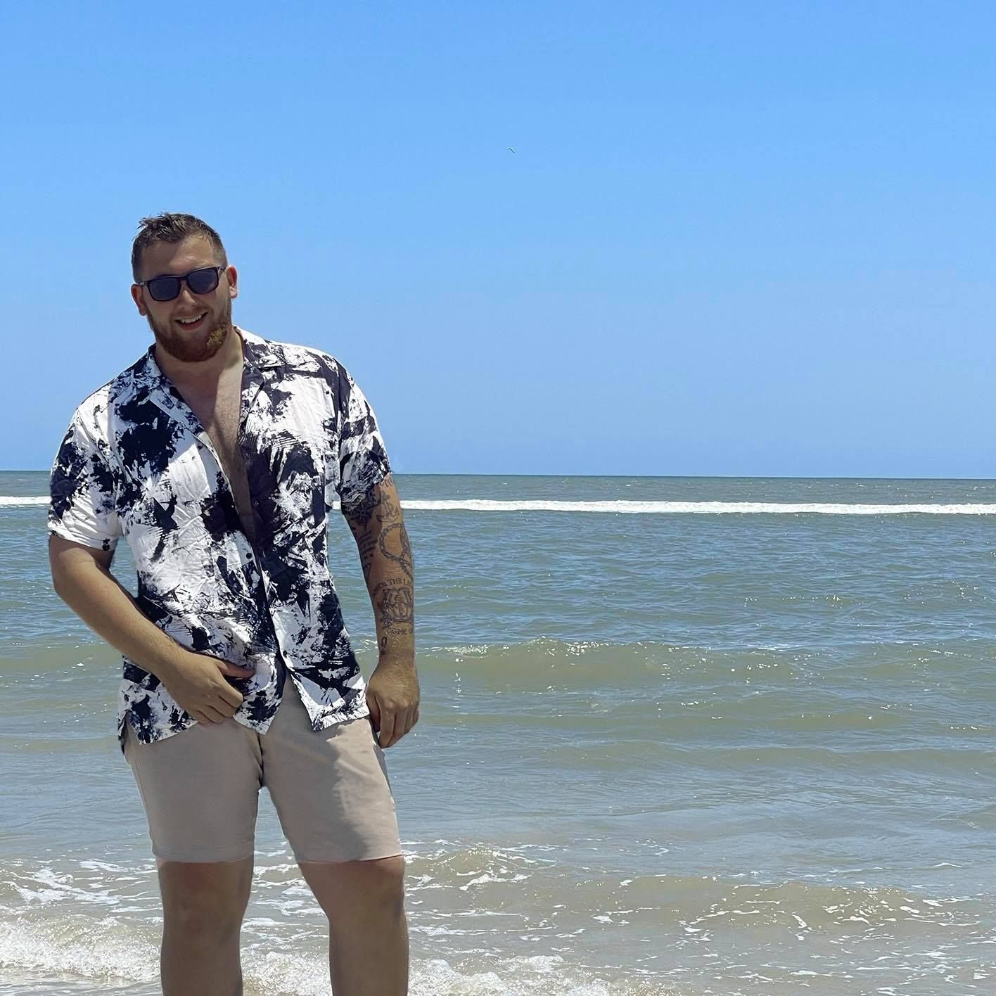 A man in a tie dye shirt is standing on the beach