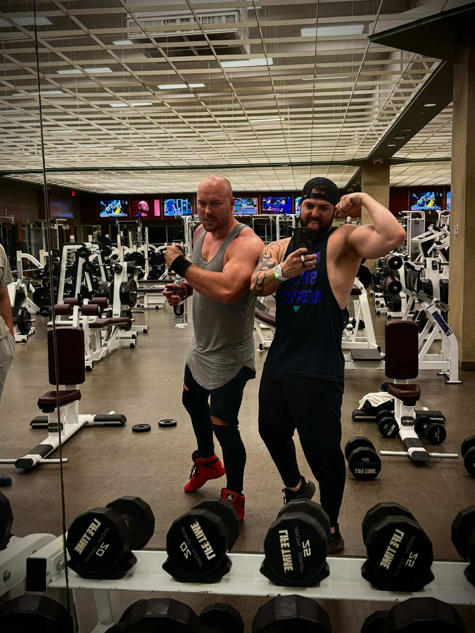 Two men are posing for a picture in a gym.