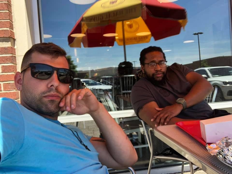 Two men are sitting at a table with an umbrella in the background
