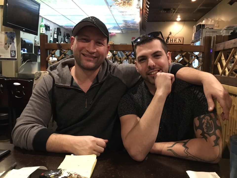 Two men are sitting at a table with their arms around each other