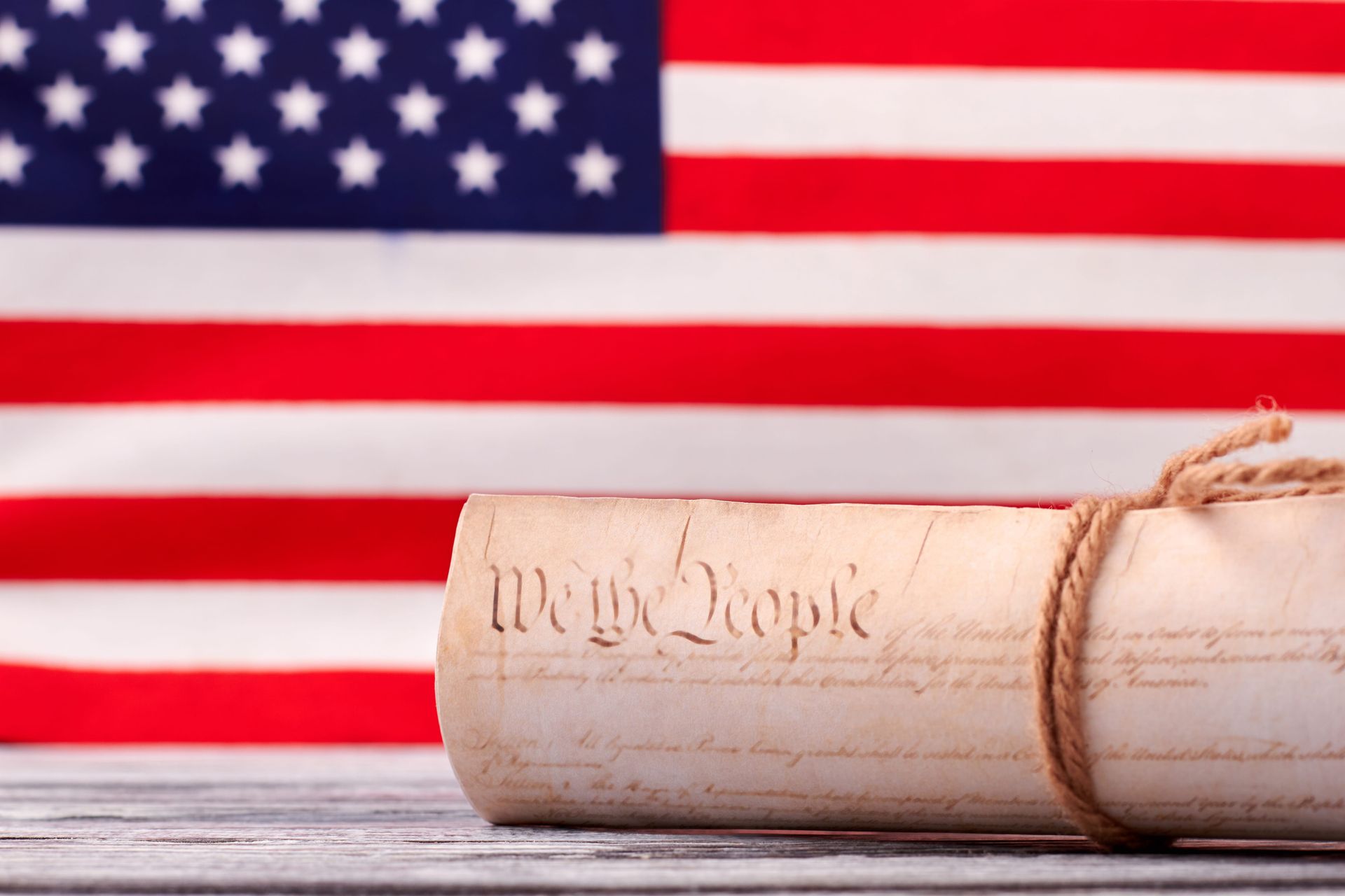 Rolled parchment labeled “We the People” in front of a U.S. flag