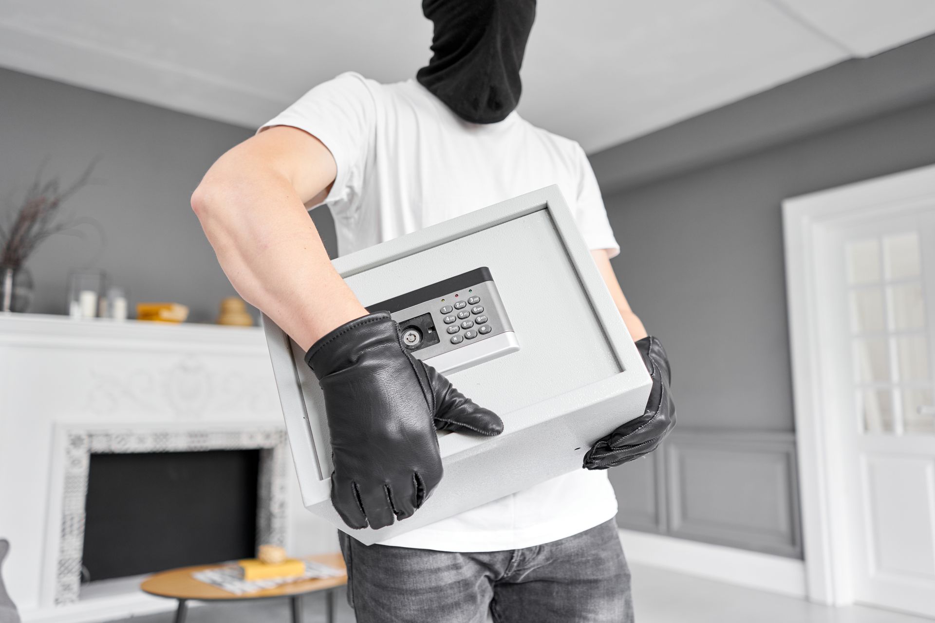 Person in black mask carrying a safe from a living room.
