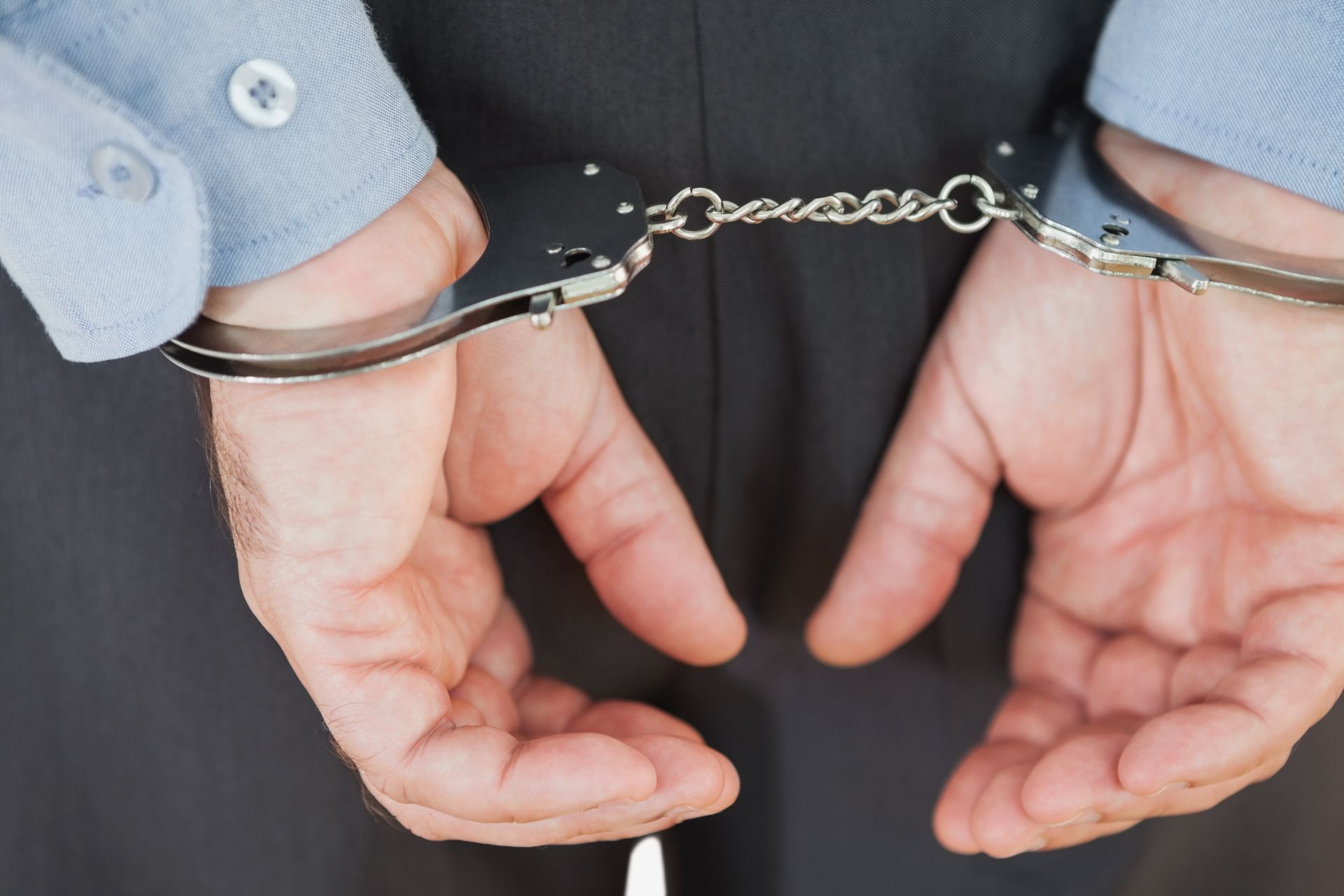 Person in light blue shirt and black pants, hands cuffed behind their back.