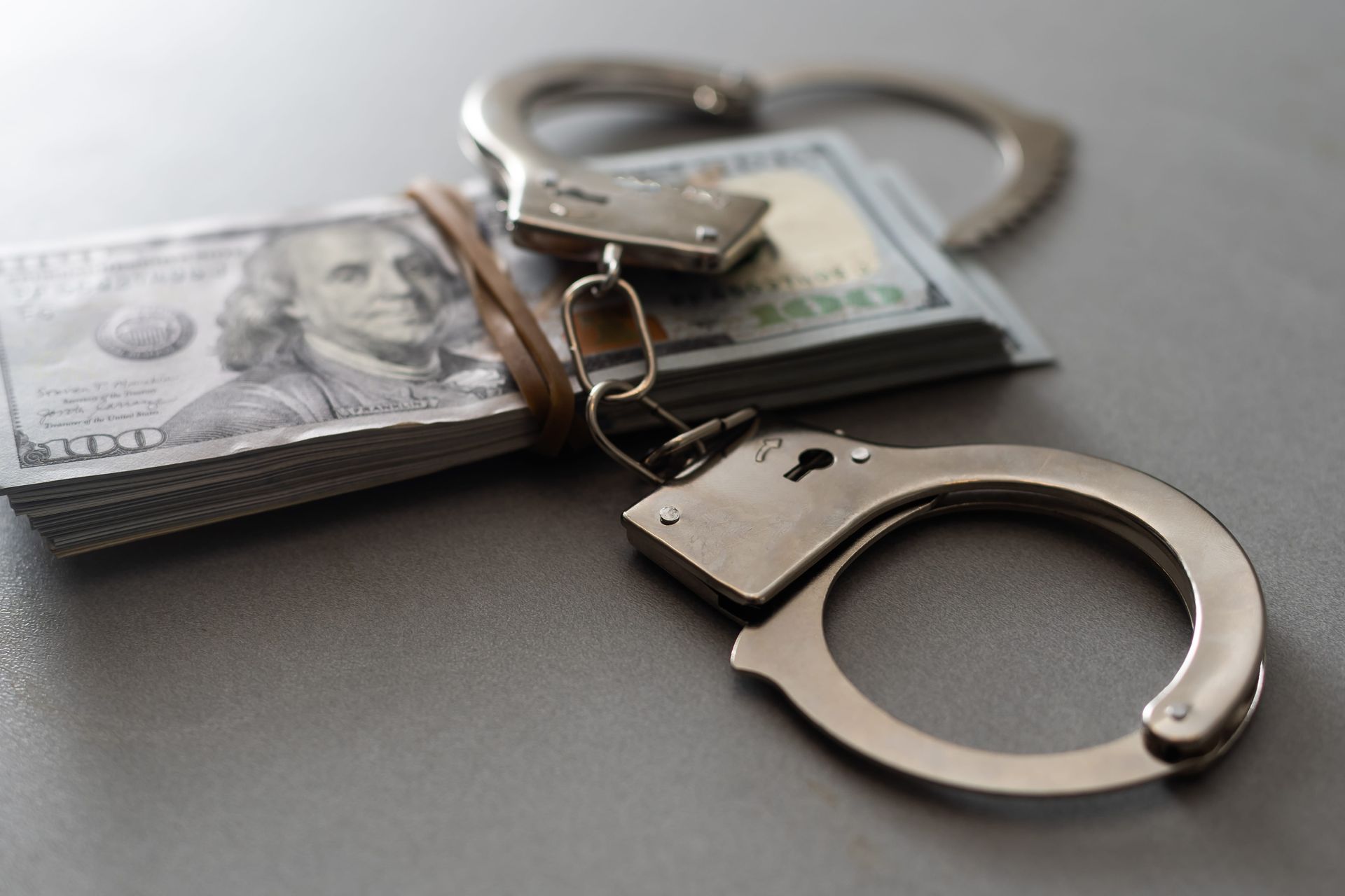 Silver handcuffs on a stack of cash, symbolizing crime and money