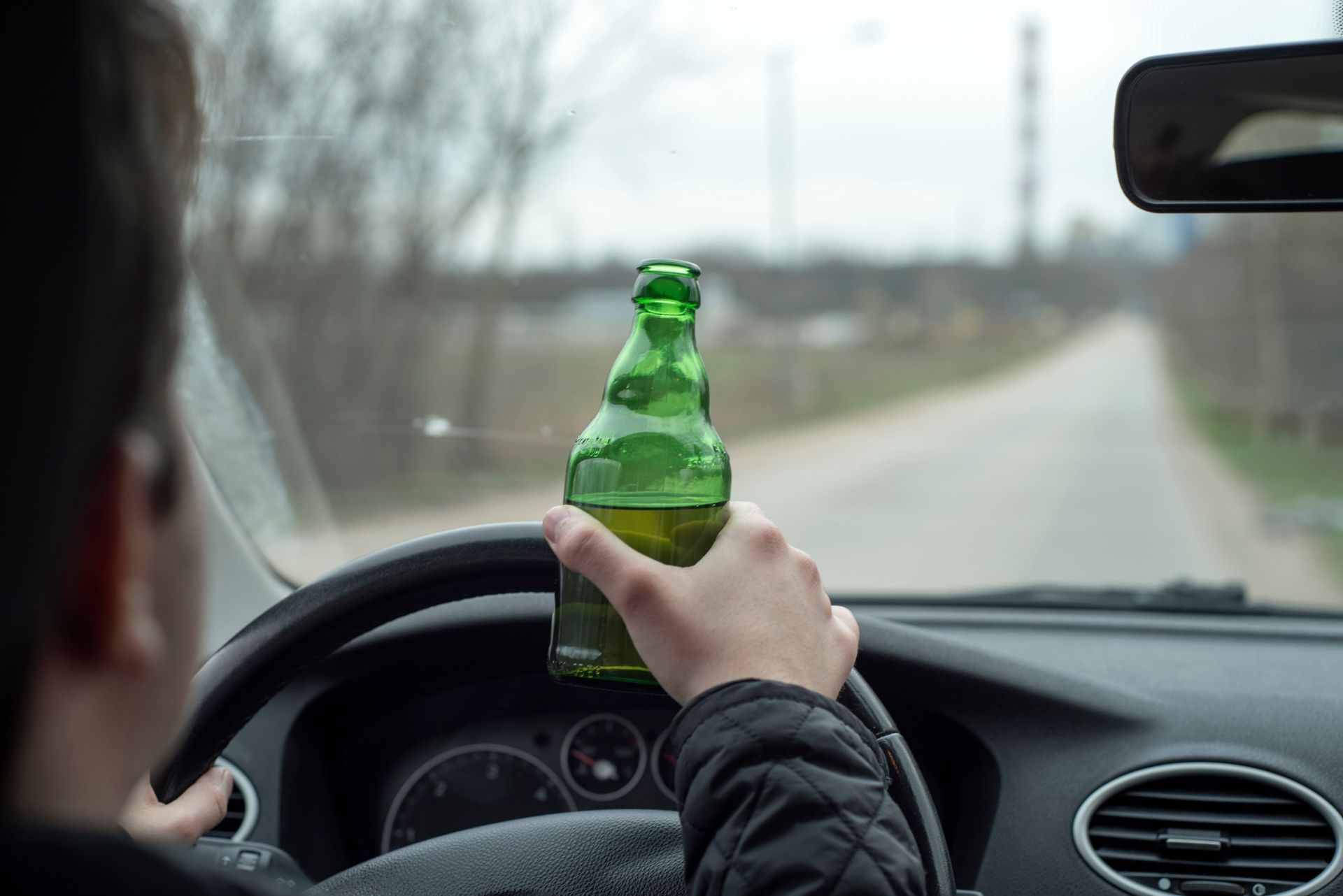 Driver holding a green bottle while steering on a rural road
