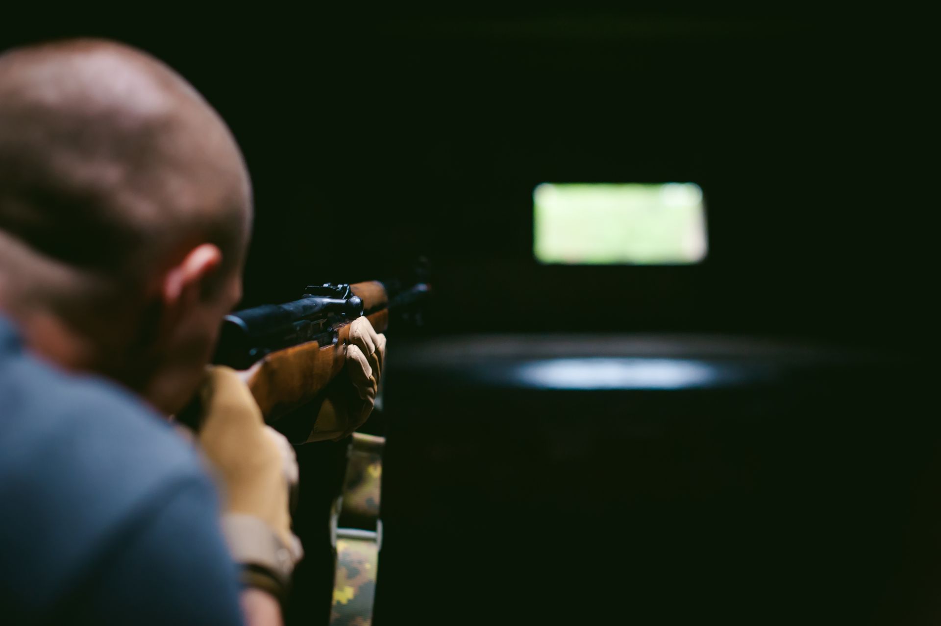 Man aims a rifle at a target in a dimly lit shooting range.