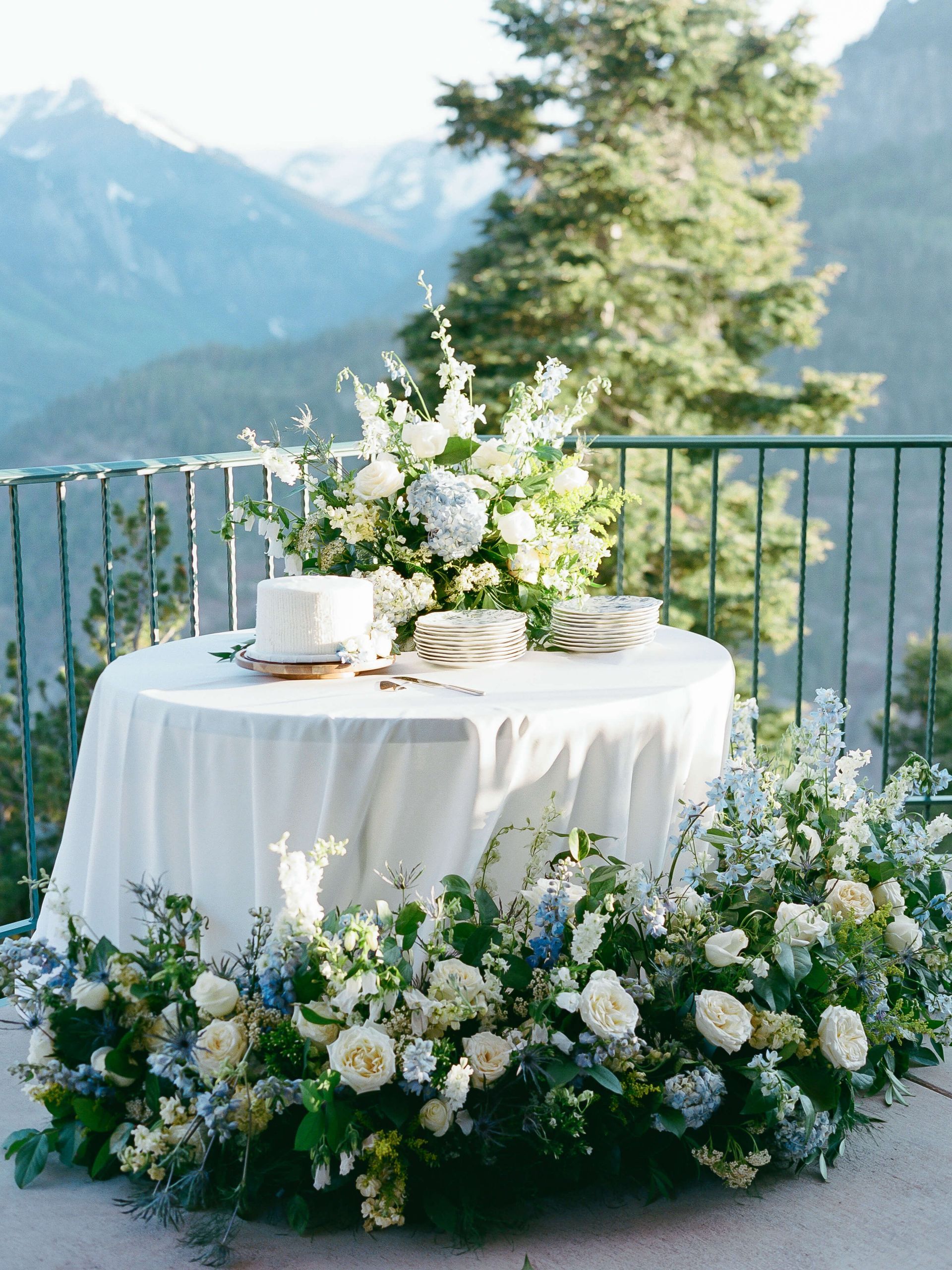 Round floral table setting on a mountain terrace with white flowers and a white tablecloth