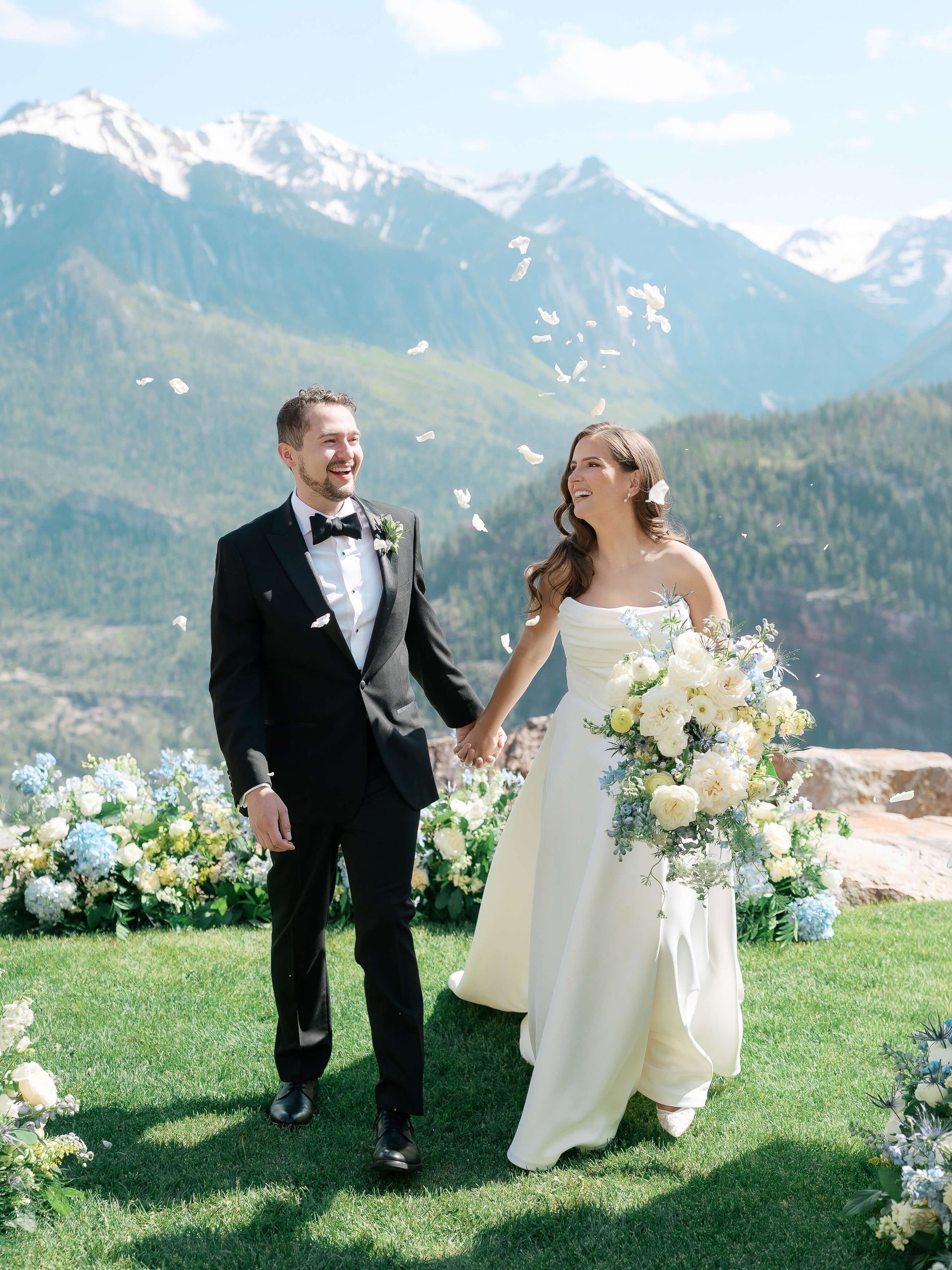 Bride and groom holding hands in a mountain meadow with snowy peaks behind them