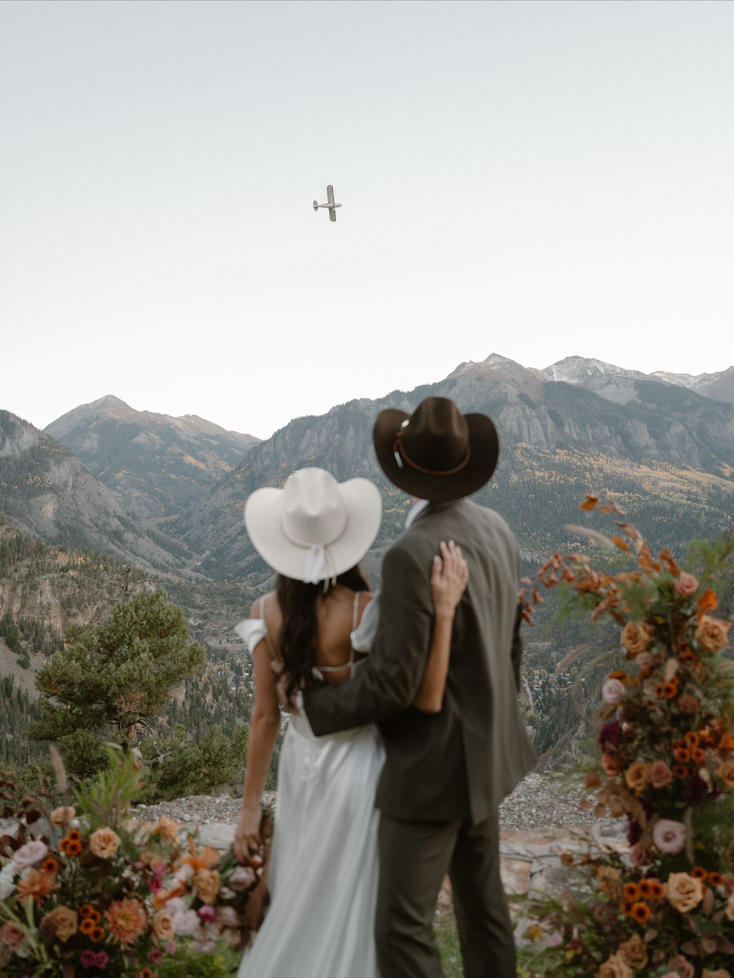 A bride and groom are kissing in a field with mountains in the background.