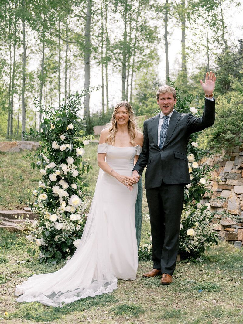 A bride and groom are standing next to each other in front of a floral arch.