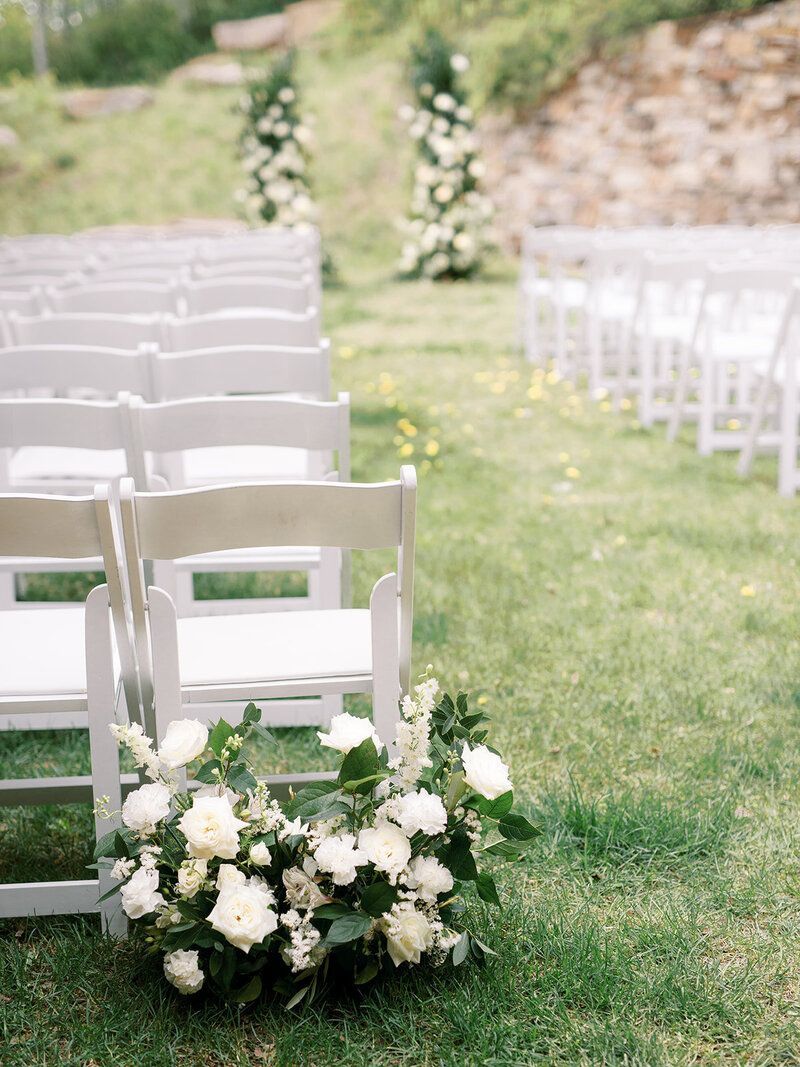 A row of white folding chairs are lined up in a grassy field.
