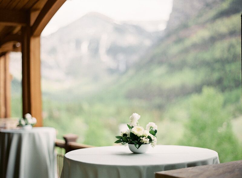 A table with a vase of flowers on it with mountains in the background.