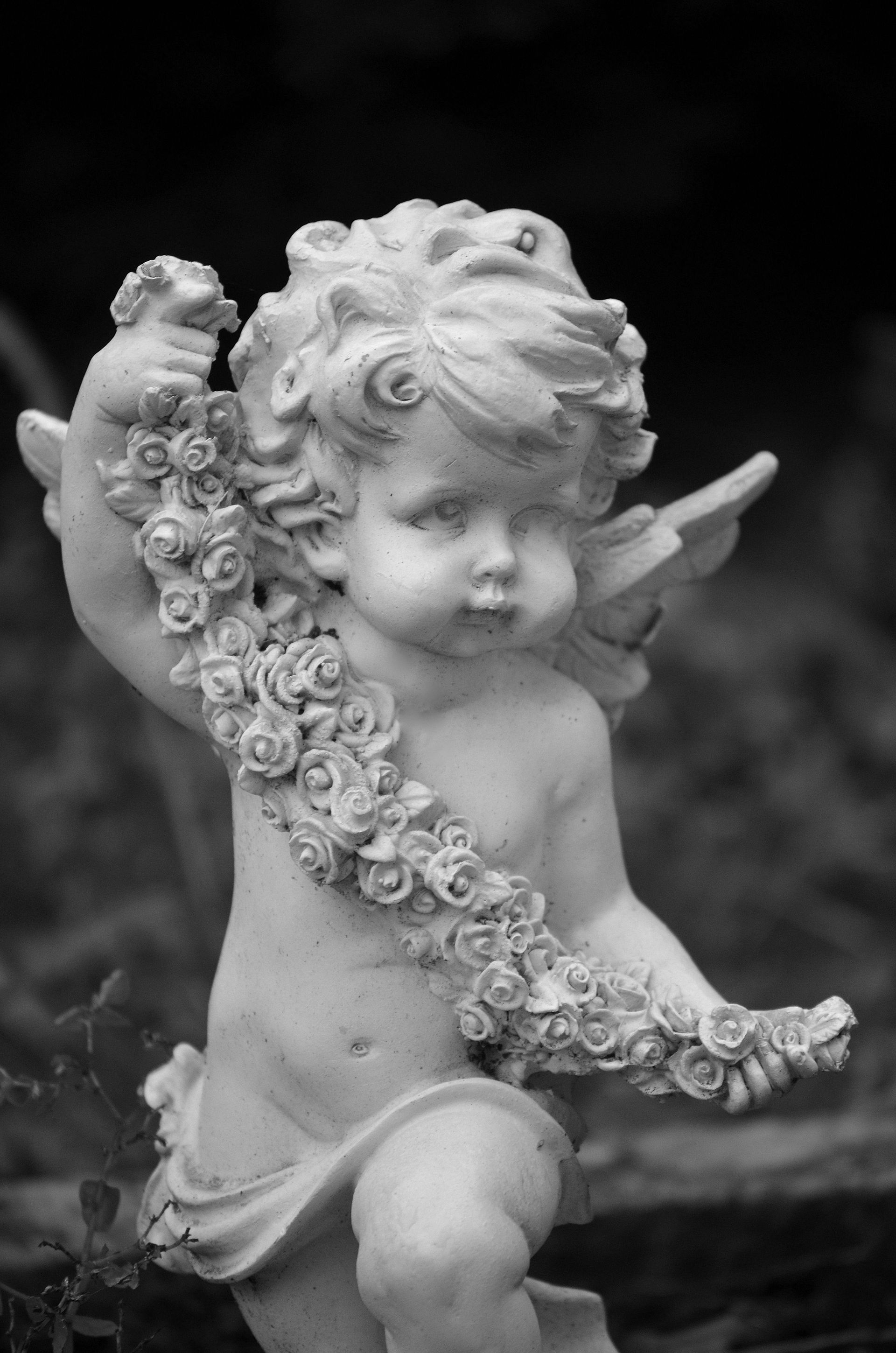 Cherubic statue holding a garland of flowers, outdoor setting.