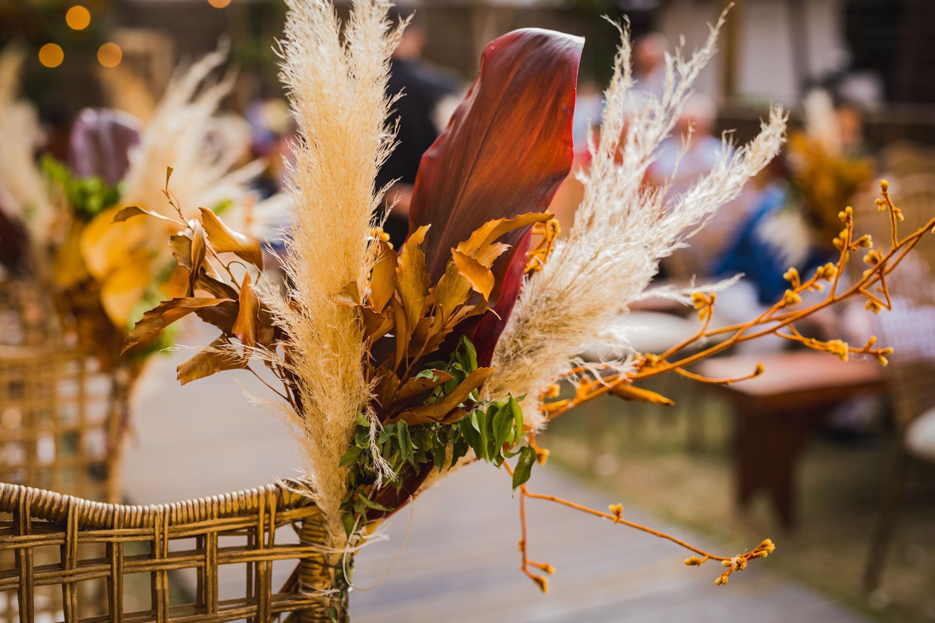 Floral arrangement with beige pampas grass and rust-colored leaves in a woven basket, softly lit indoors