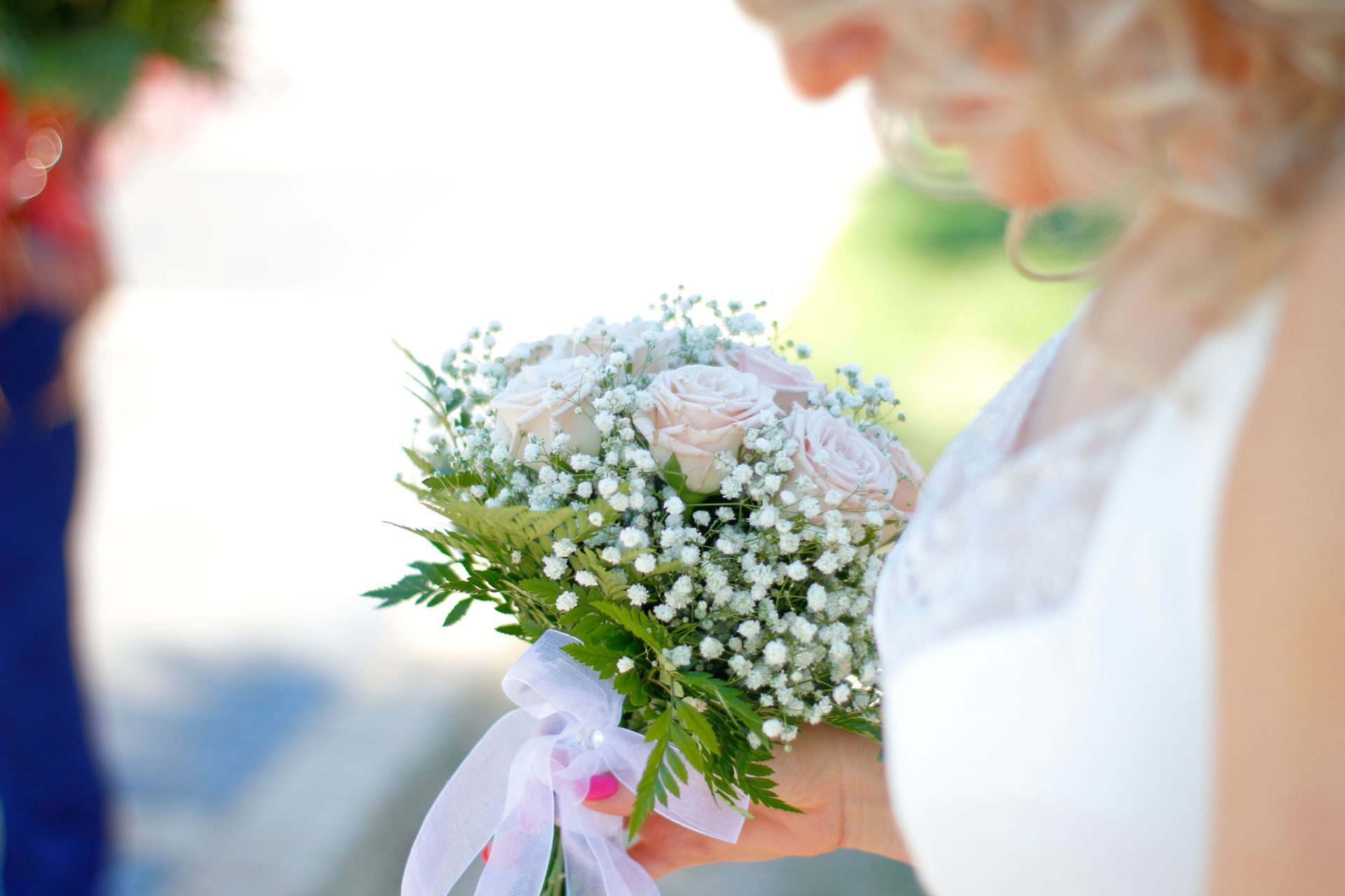 Bride holding a white and pink bouquet with baby's breath in a bright outdoor setting