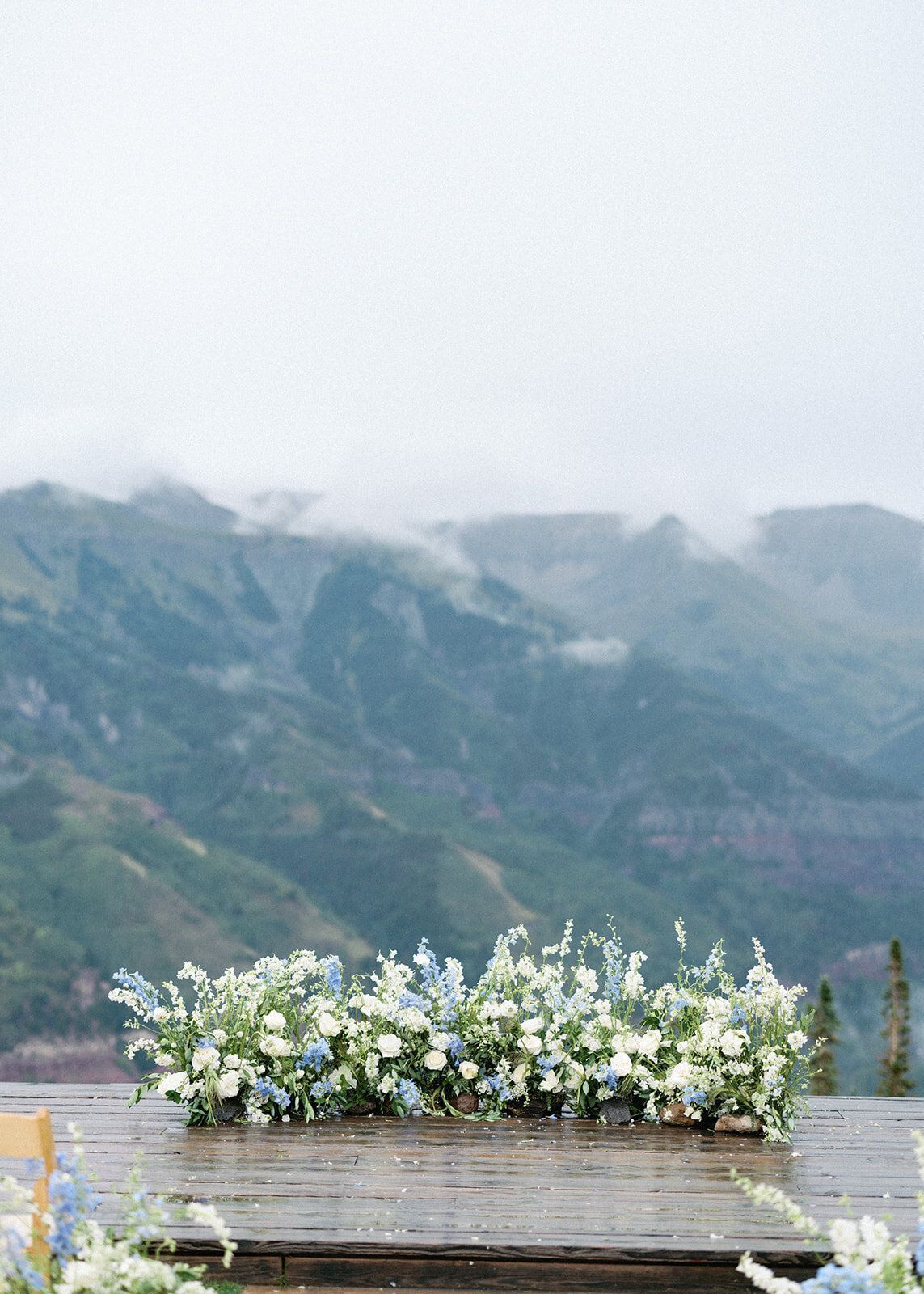 A wooden table with flowers on it in front of a mountain range.
