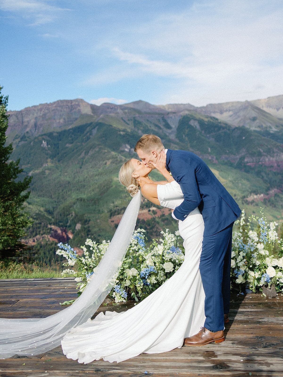 A bride and groom are kissing in front of mountains.