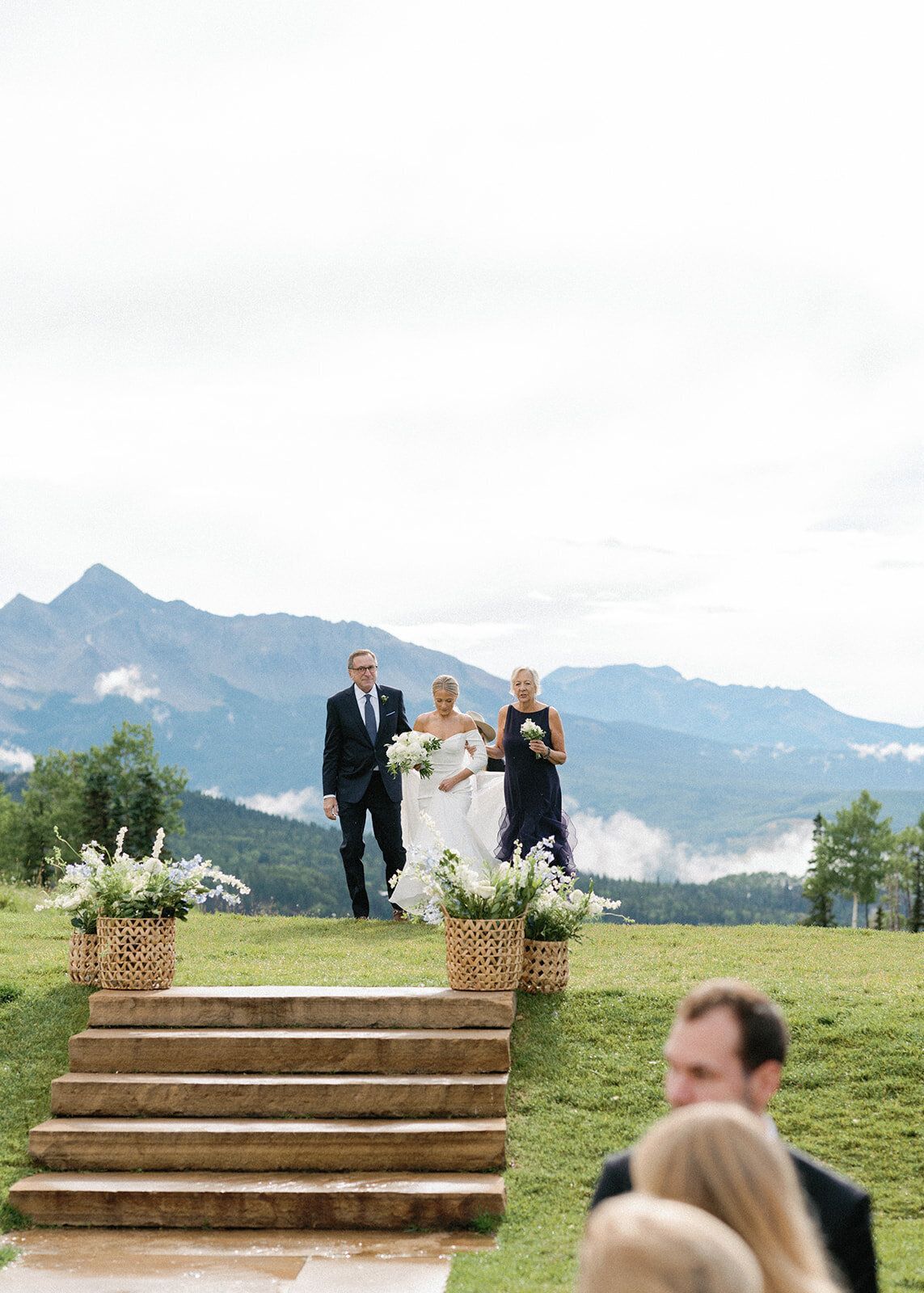 A bride and groom are walking down the aisle at a wedding with mountains in the background.