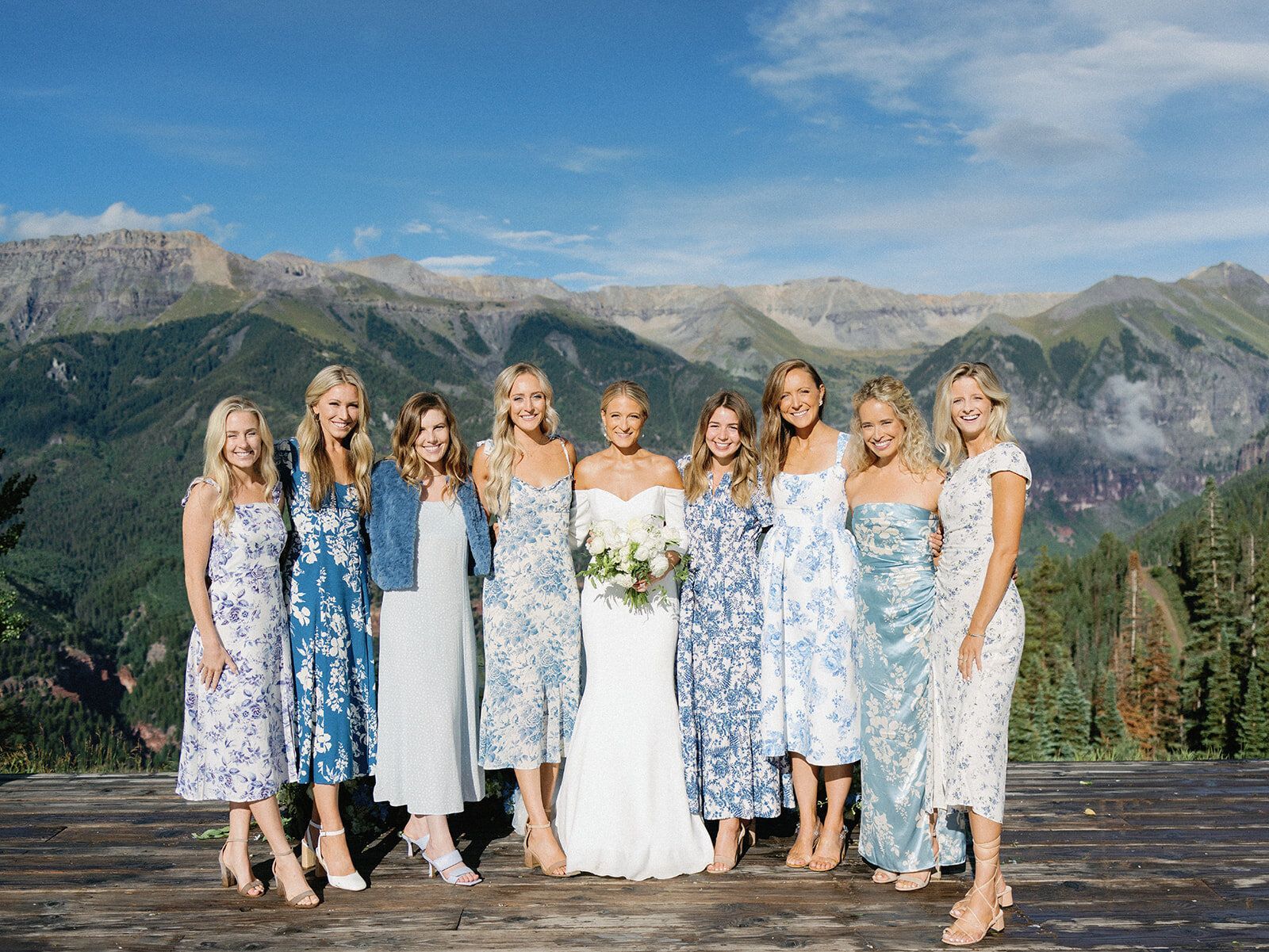 A bride and her bridesmaids are posing for a picture with mountains in the background.