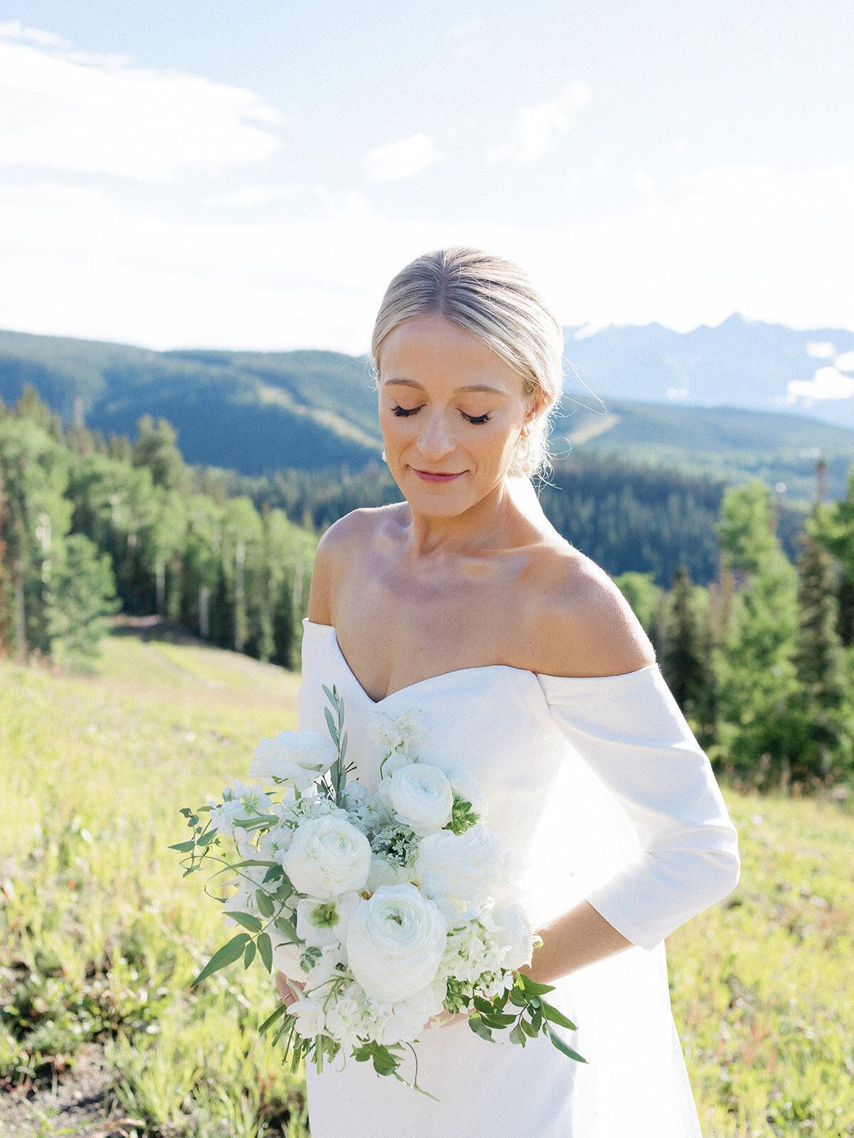 A bride in a white dress is holding a bouquet of white flowers in a field.
