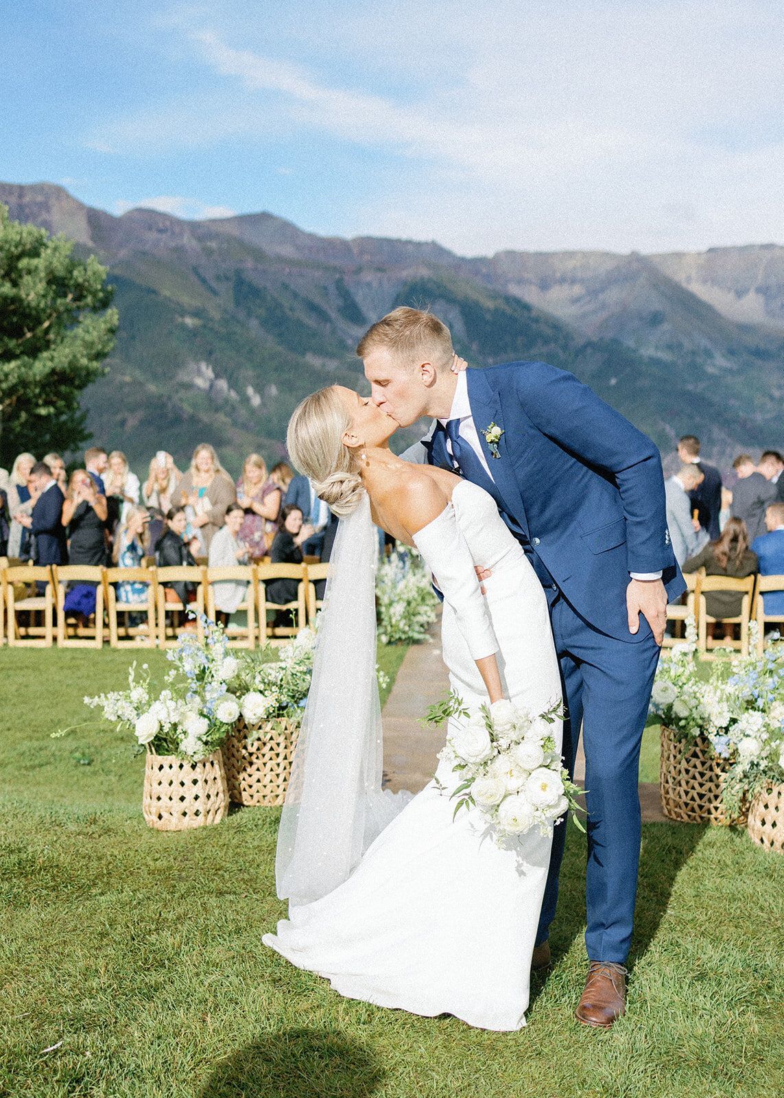 A bride and groom are kissing in front of their wedding guests.