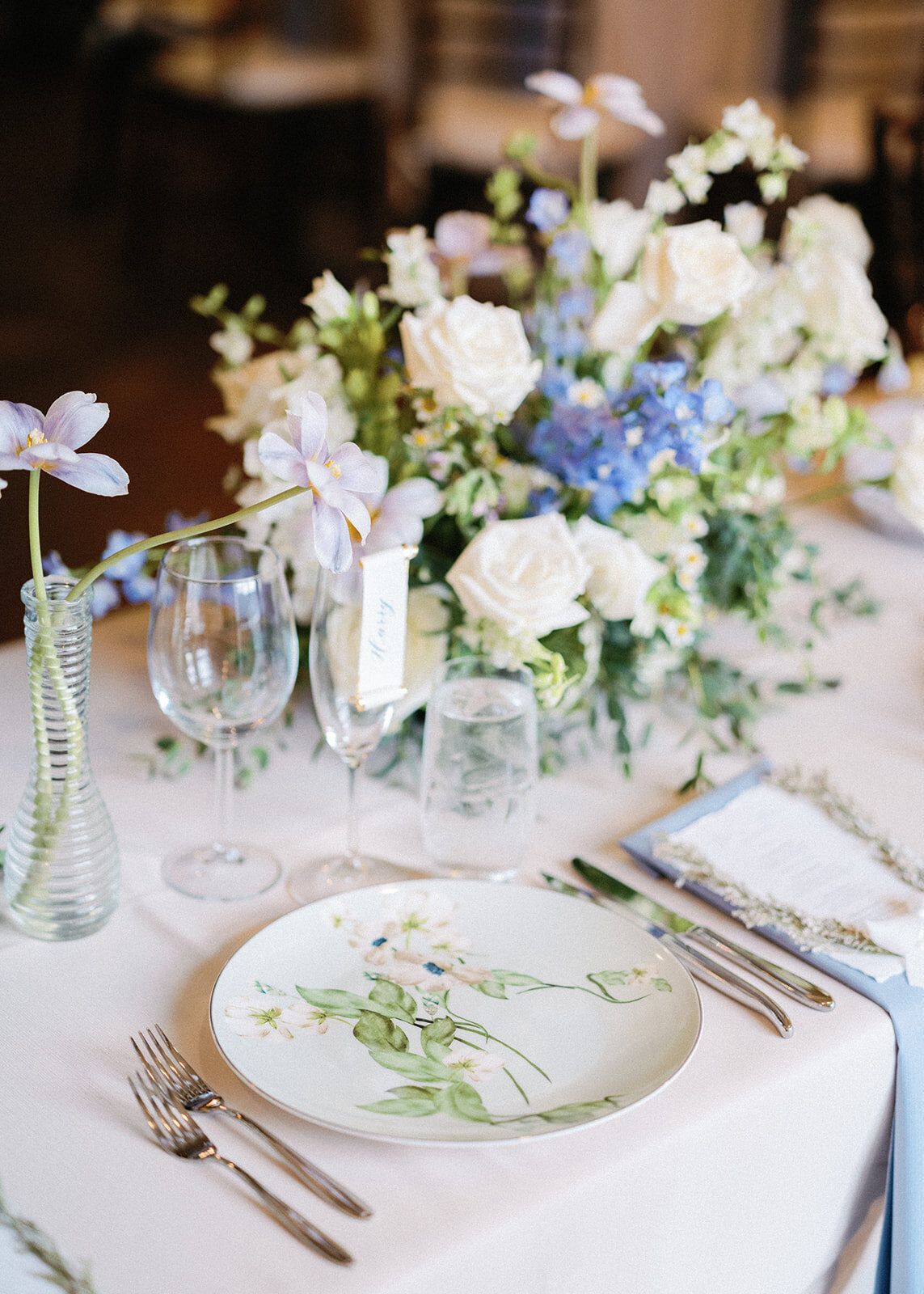 A table with plates , utensils , and a vase of flowers on it.