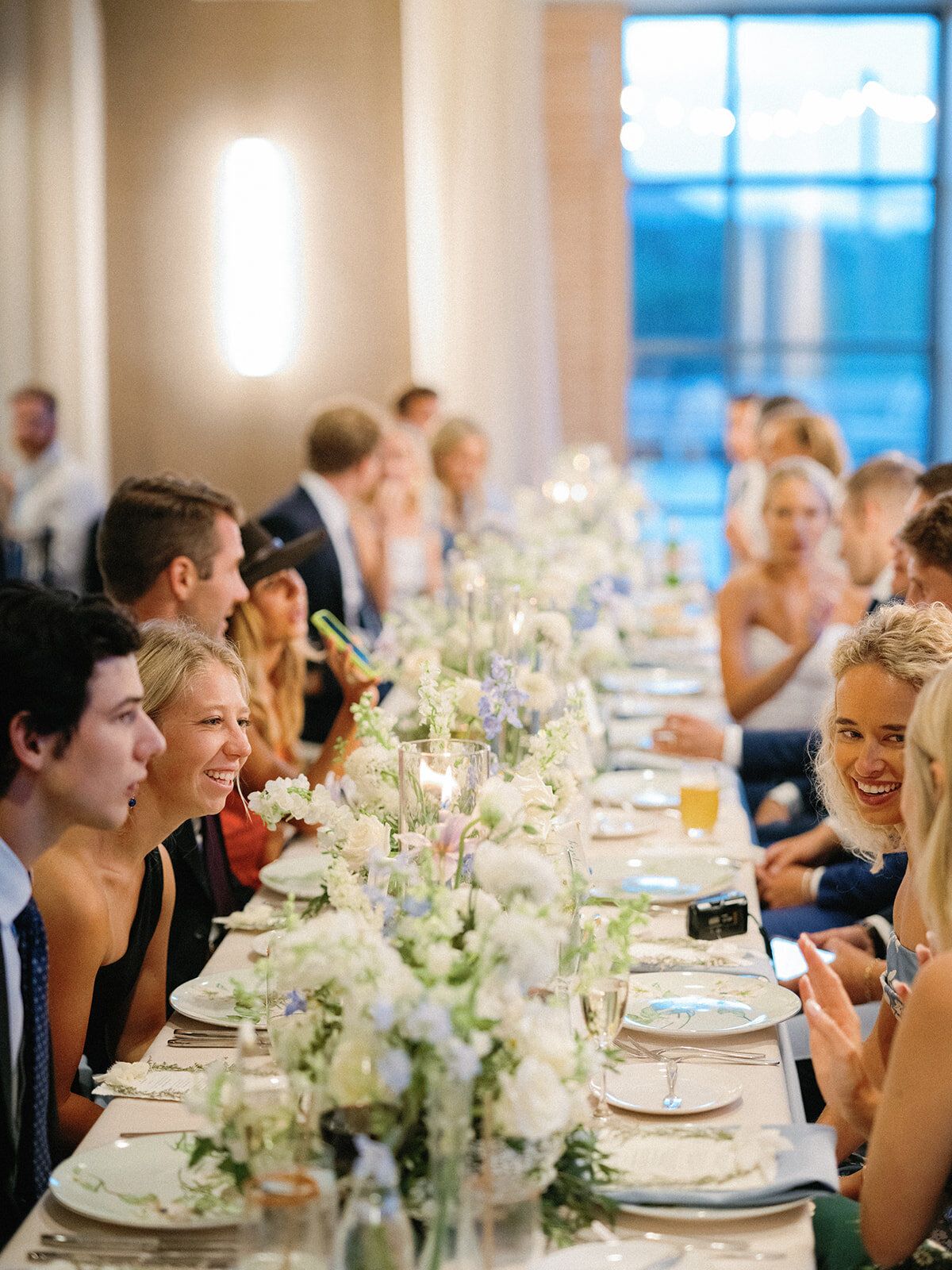 A group of people are sitting at a long table at a wedding reception.