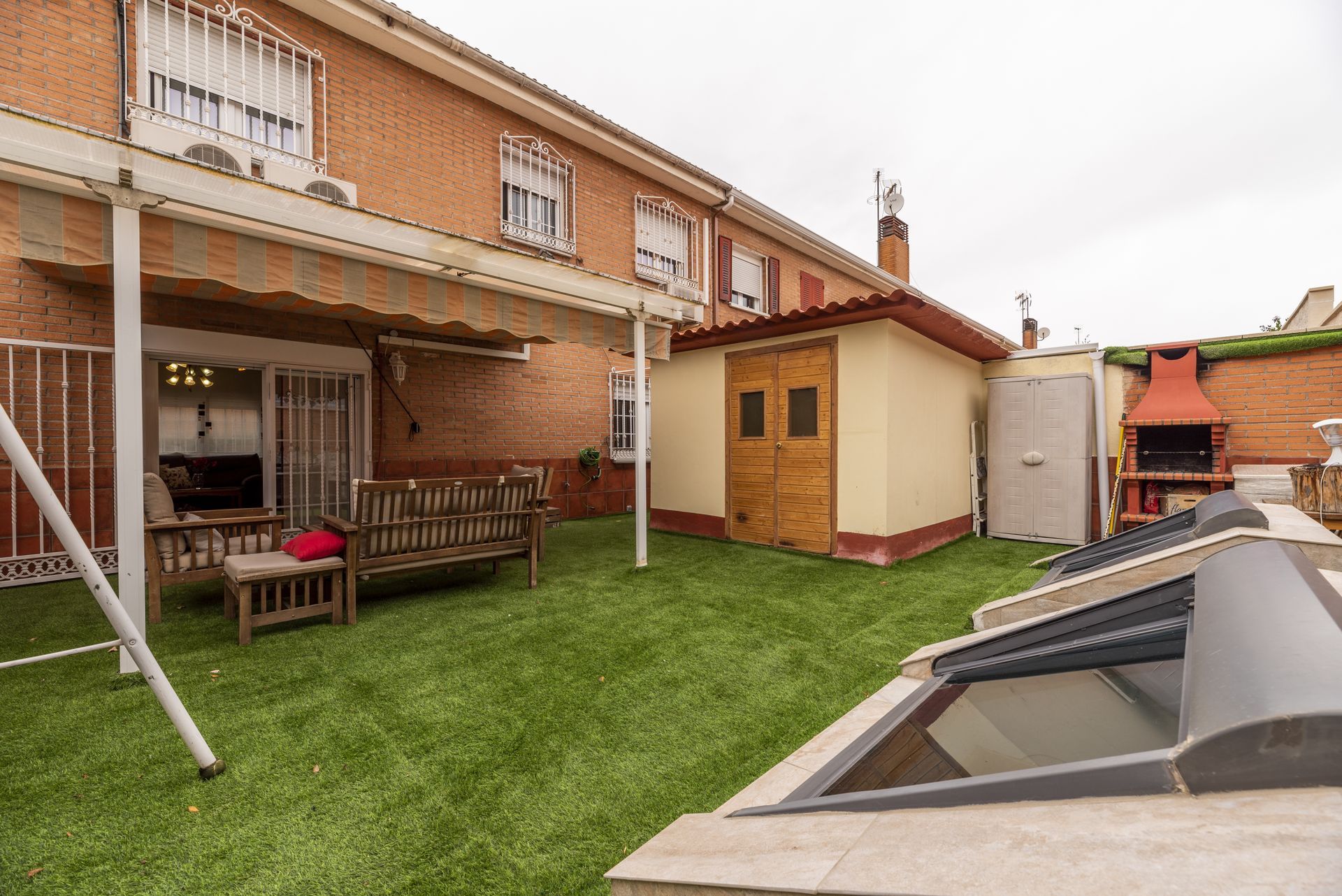 Backyard patio with grass, covered seating, shed, and a covered pool beside a brick house