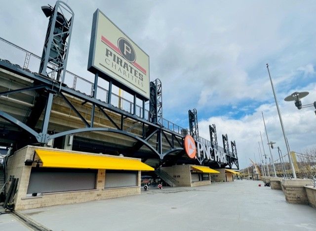 Exterior of PNC Park, home of the Pittsburgh Pirates, with closed concession stands, yellow awnings, and a cloudy sky.