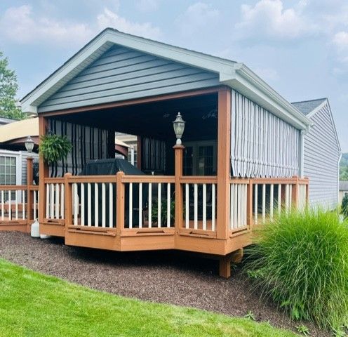Covered wooden deck with retractable striped shades and railing, attached to a house.