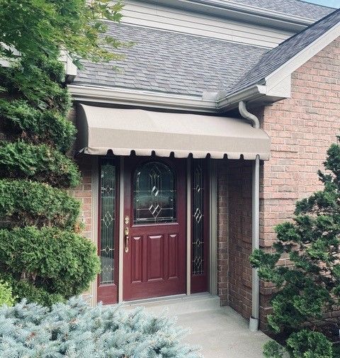 A beige awning over a red door. Brick exterior, bushes frame the entrance.
