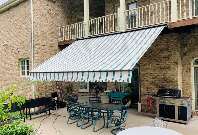 Patio with awning; striped blue and white canopy, outdoor dining set, and brick building exterior.