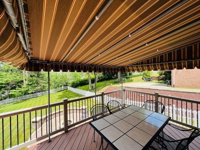 Deck with retractable awning, table, and chairs overlooking a yard with a white fence.