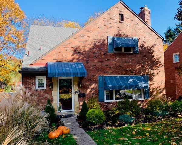 Red brick house with blue awnings and autumn foliage.