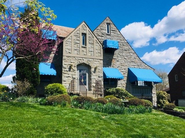 Stone house with blue awnings on a grassy hill under a blue sky with clouds.