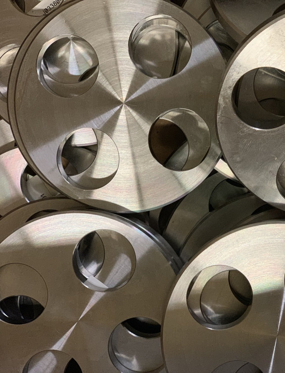 Stack of metal discs with four circular cutouts, reflecting light.