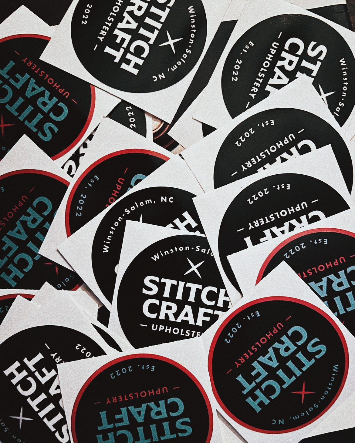 Assorted black-and-white circular Stitch Craft logo stickers with red accents scattered on a white surface