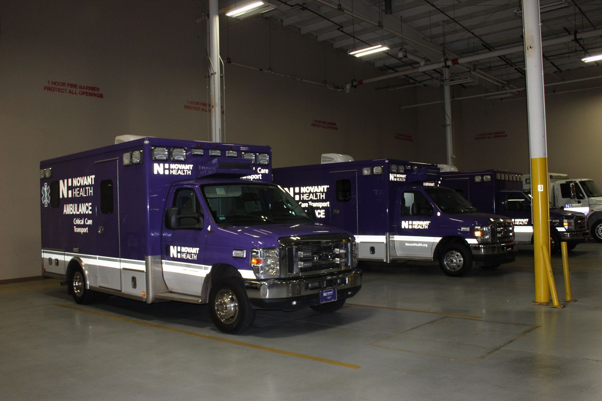 Three purple-and-white armored vans parked inside a warehouse garage