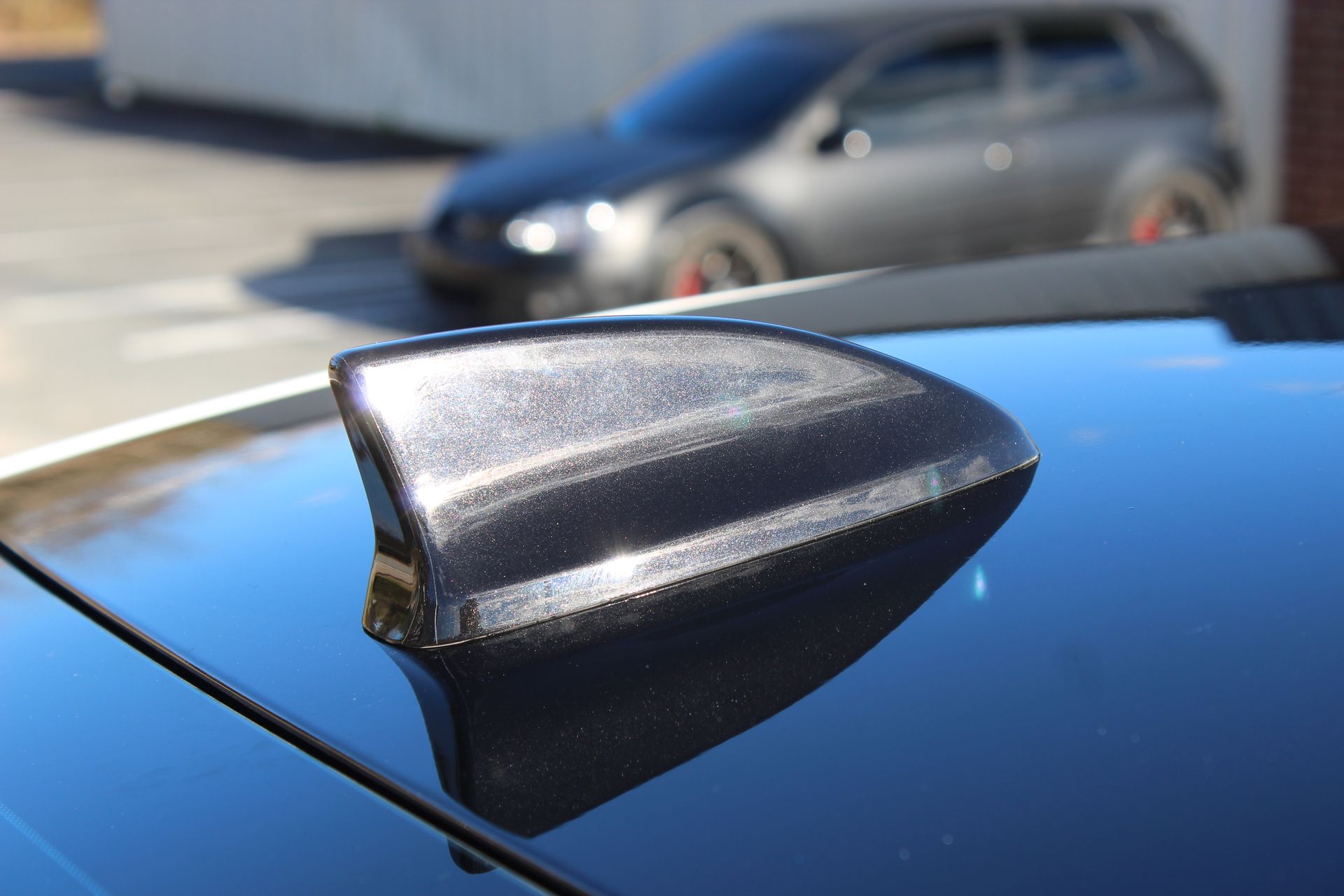 Black car shark-fin antenna on a blue roof, with a blurred silver car in the background