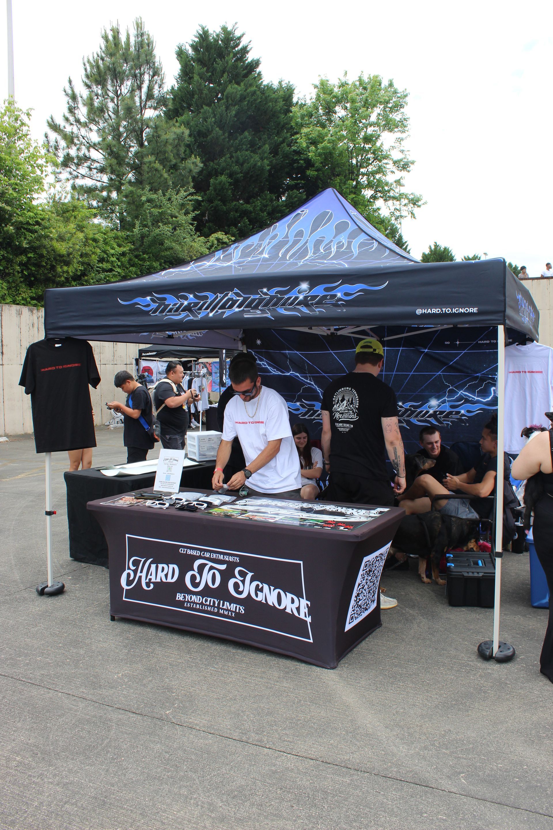 Outdoor vendor booth with black canopy and table displaying T-shirts and merchandise at an event