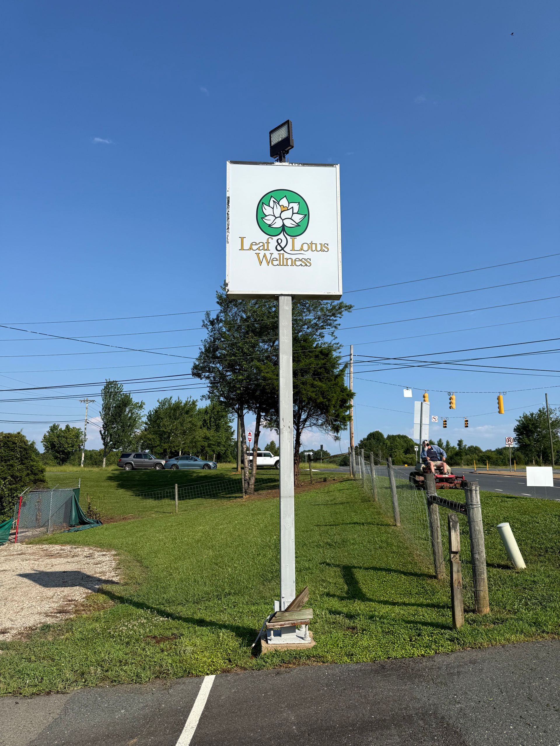 White signpost with green logo beside grassy roadside under a clear blue sky