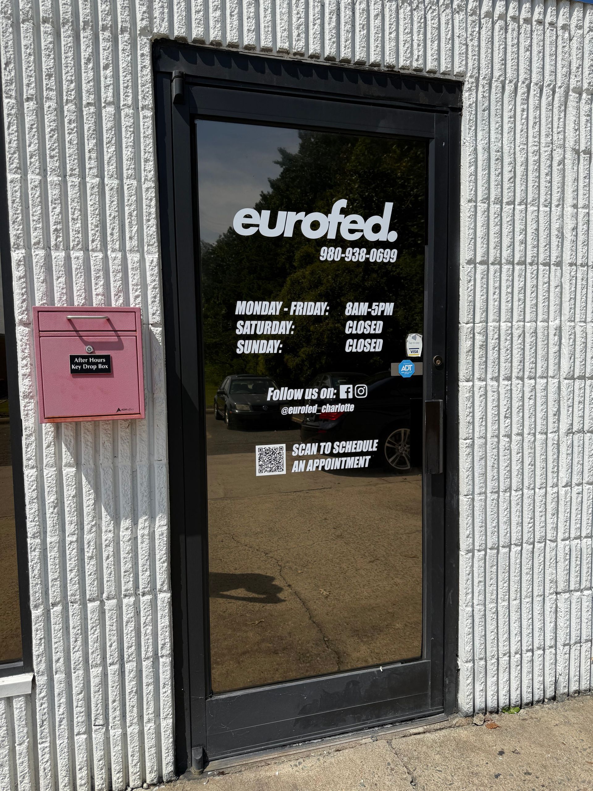 Glass storefront door for Eurofed with black frame, business hours, and a pink mailbox beside it