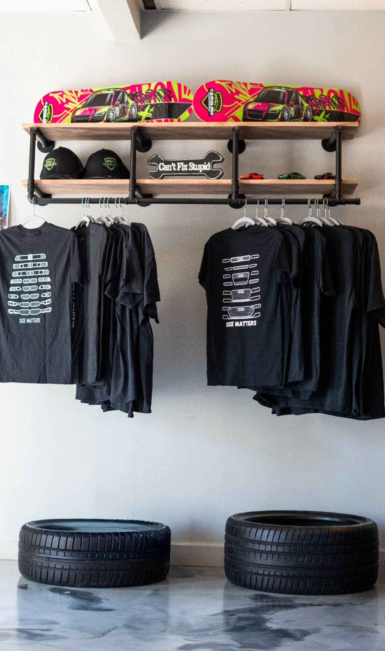 Clothing display with black T-shirts and jackets hanging on wall shelves, colorful skateboards on top, tires below