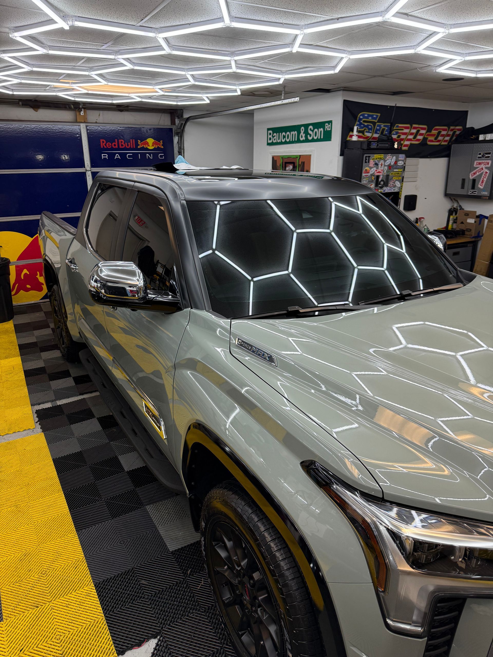 Silver SUV in a showroom, with a black roof and bright hexagonal ceiling lights reflected on the windshield