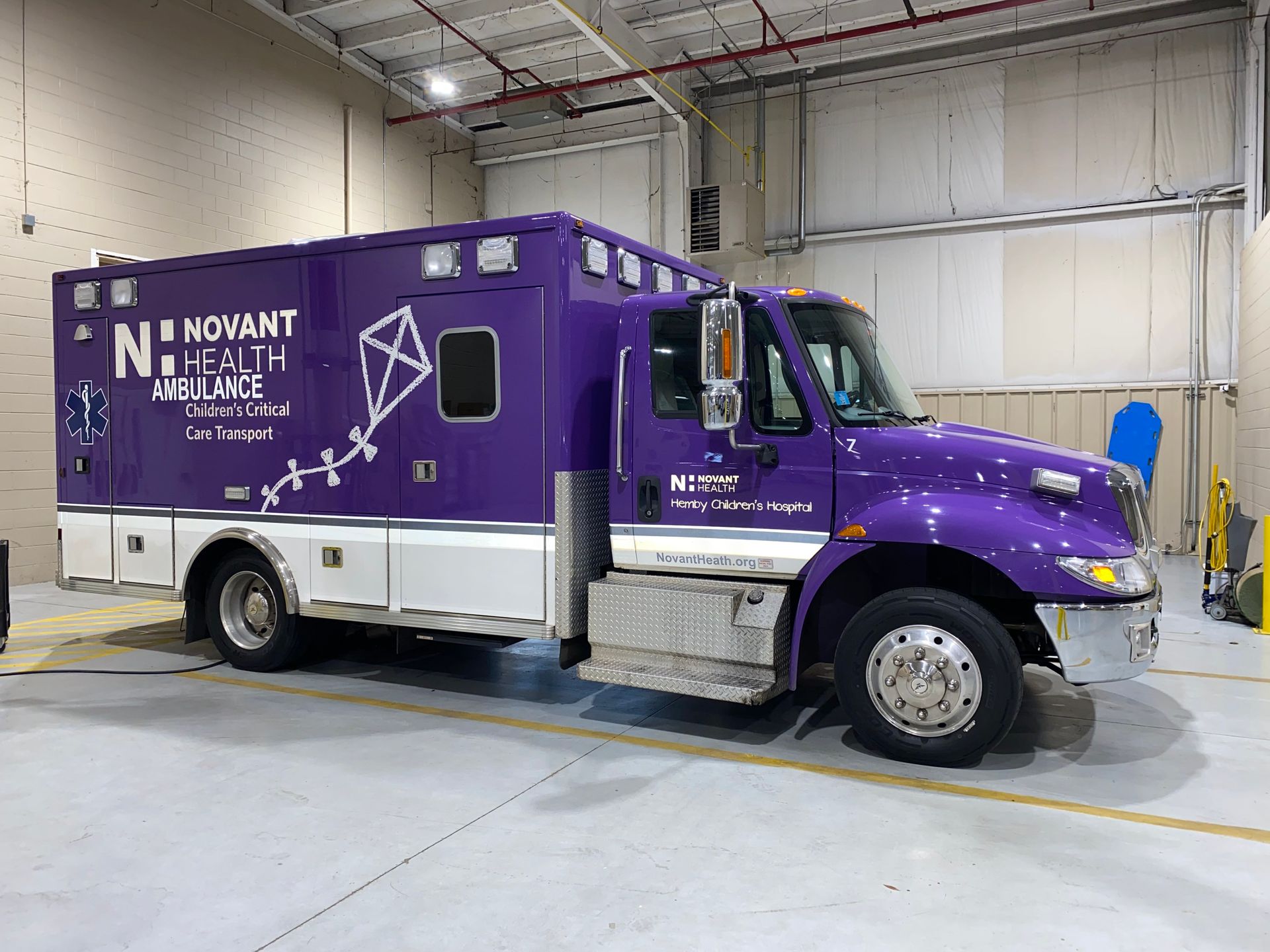 Purple and silver mobile health clinic van parked indoors in a warehouse or garage.