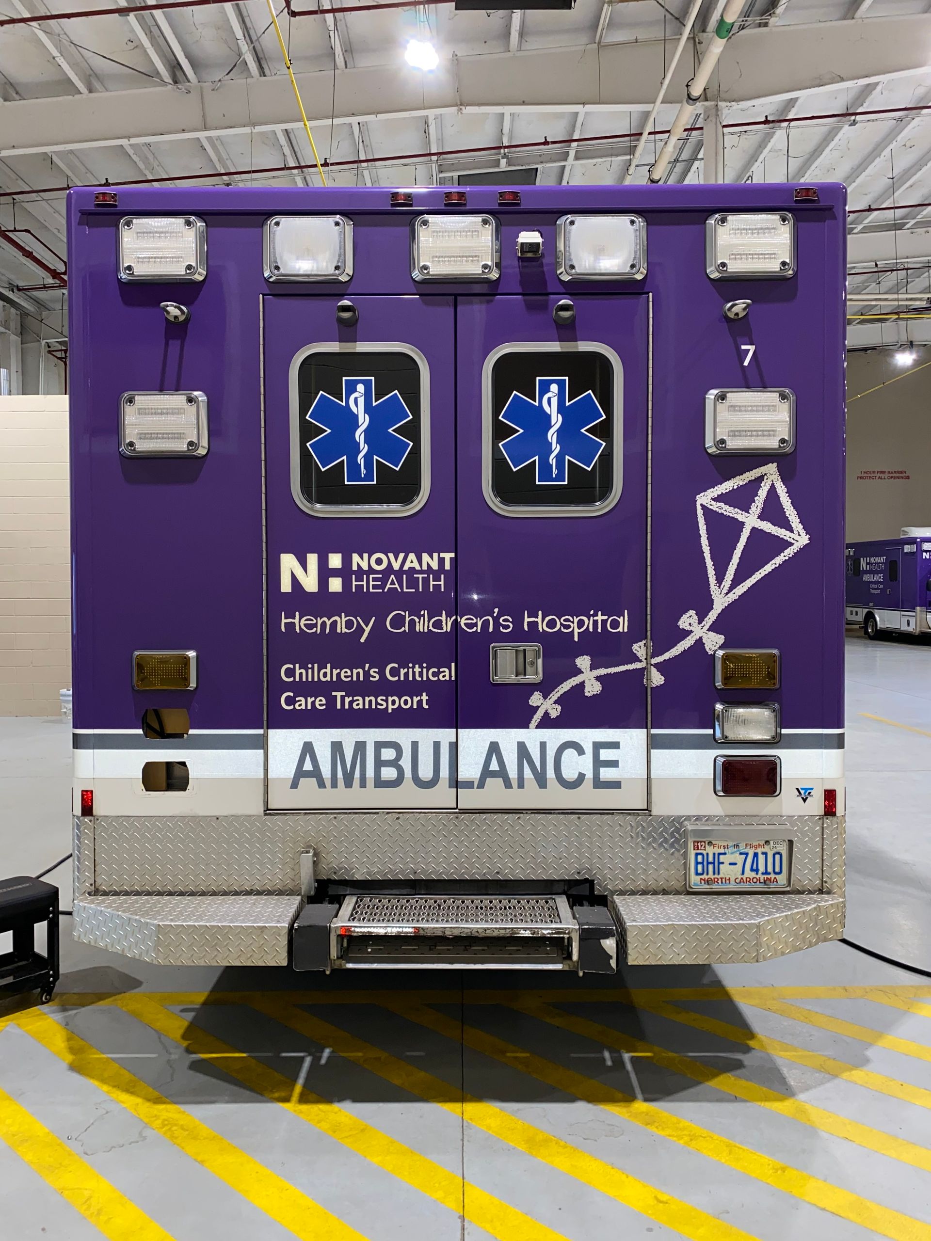Purple ambulance rear with blue Star of Life symbols parked on a marked roadway.