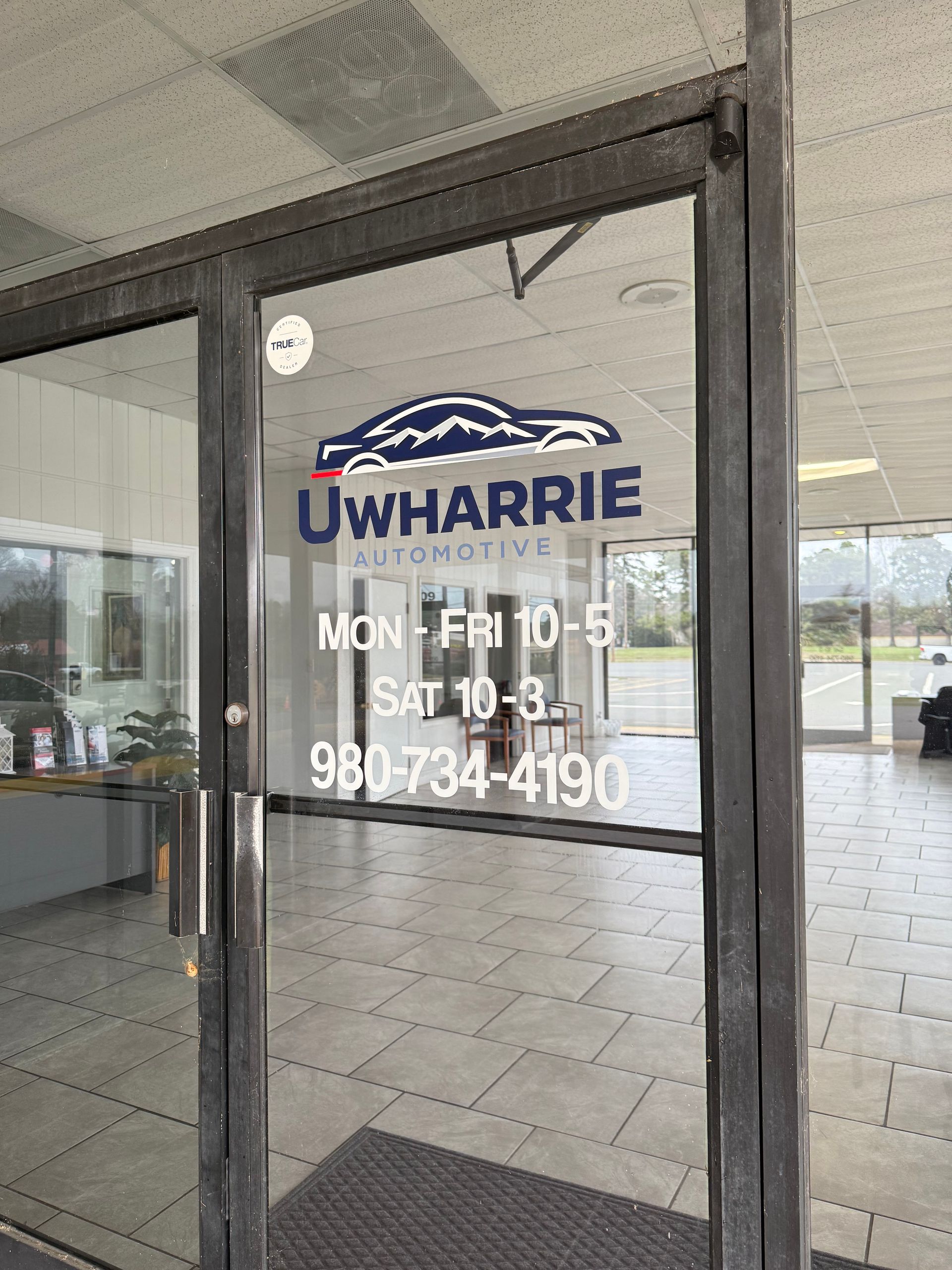 Storefront glass door with Uwharrie logo, visible interior, and hours/phone number in white lettering