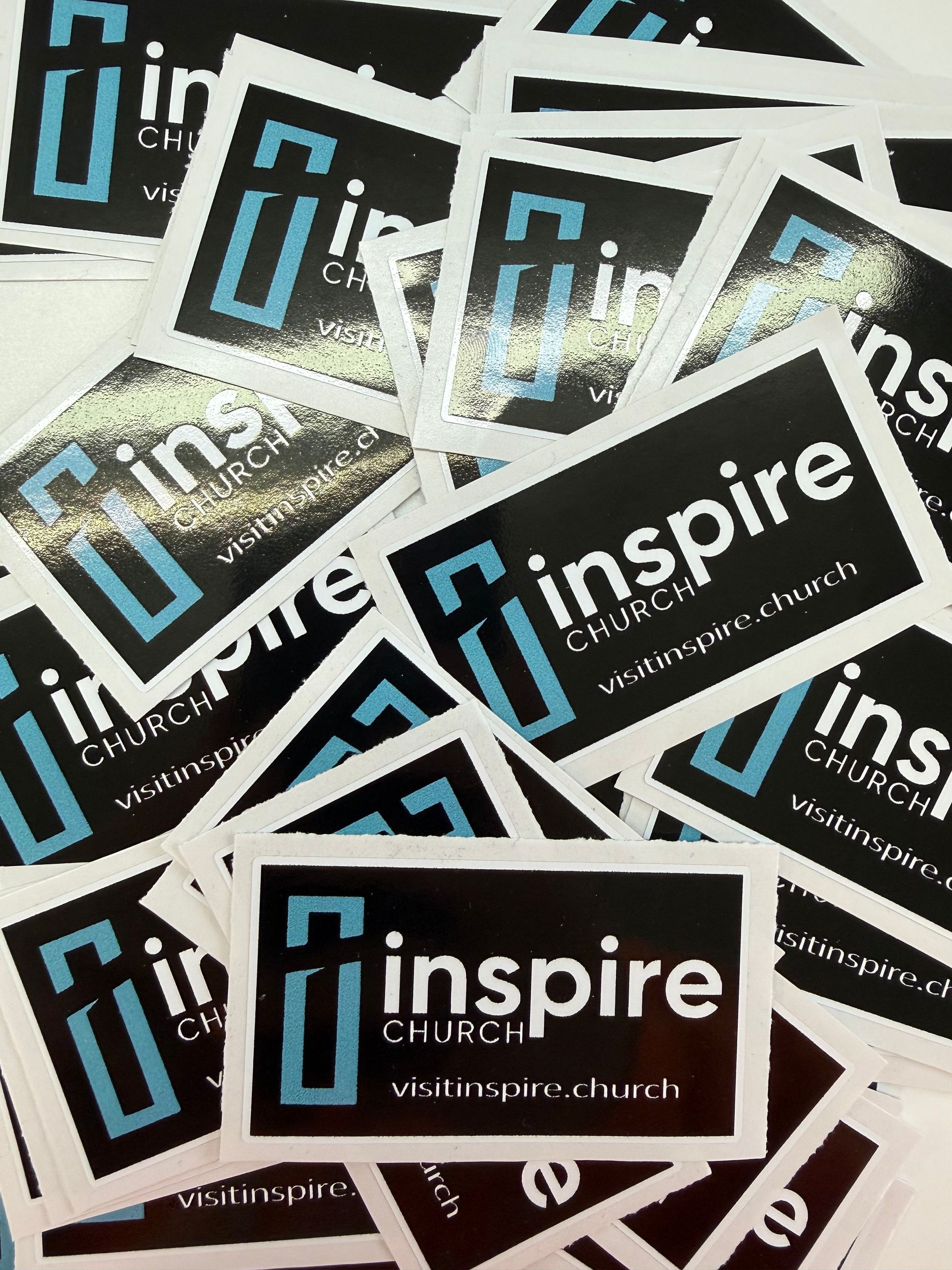 Stack of black-and-white “inspire” church cards with blue lettering scattered on a surface